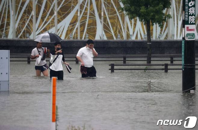 일본 규슈 후쿠오카현 남서부 구루메시에 내린 폭우로 강이 범람하면서 물에 잠긴 도로를 7일 주민들이 건너고 있다.  © AFP=뉴스1