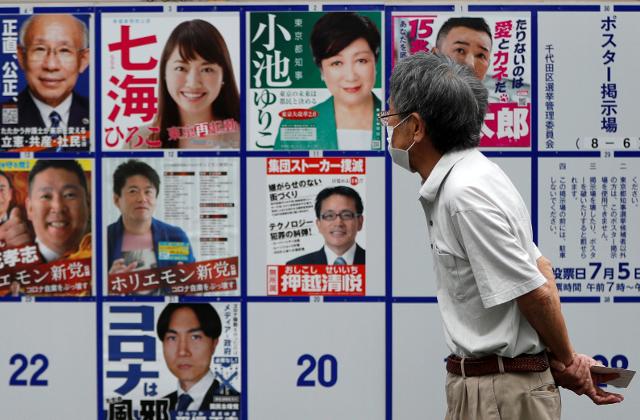 지난 5일 치러진 일본 도쿄도지사 선거에 앞서 마스크를 착용한 남성 유권자가 시내에 설치된 선거포스터 게시판 앞을 지나가고 있다. 도쿄=로이터 연합뉴스
