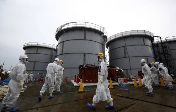 방호복과 방사능 차단 마스크를 착용한 일본 도쿄전력 직원들이 후쿠시마현 오쿠마에 있는 후쿠시마 제1원자력발전소에서 방사능 오염수가 저장돼 있는 탱크 주변을 지나고 있다.오쿠마 AP 연합뉴스