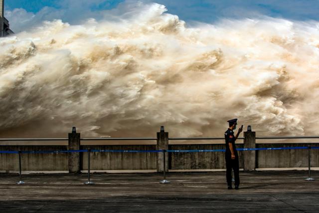 지난달 19일 중국 후베이성 이창시에 있는 세계 최대 규모의 수력발전 댐인 쌴샤댐이 방류중인 가운데 마스크를 쓴 한 공안이 휴대폰으로 촬영을 하고 있다. 이창=AFP 연합뉴스