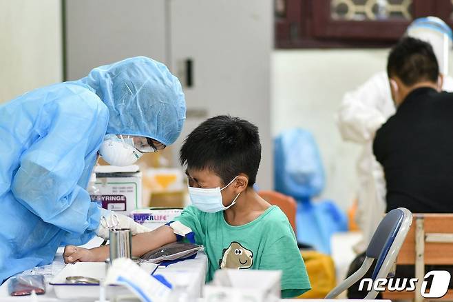 1일 베트남 하노이의 선별 진료소에서 보호복을 입은 의료진이 코로나19 검사를 위해 소년의 혈액 샘플을 채취하고 있다. © AFP=뉴스1