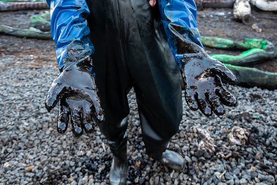 15일 모리셔스 해안에서 기름 제거 작업에 나선 현지 주민이 작업복과 장갑에 묻은 원유를 보여주고 있다. EPA=연합뉴스