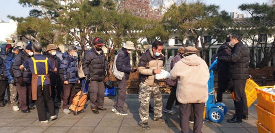 去る26日、ソウル市鍾路区タプコル公園のフェンスのそばで、マスクを使った高齢者のお弁当配食を受けるために密着して並んでいる。（写真=類テミン記者）