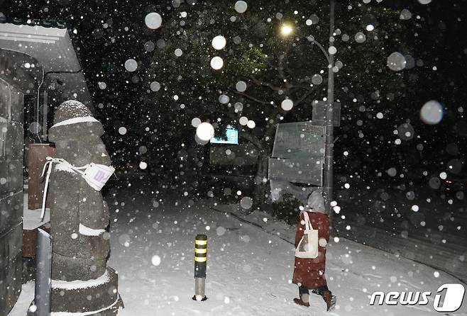 제주에 대설특보가 내려진 7일 저녁 제주시 연동 한 거리에 세워진 돌하르방 옆을 시민이 걷고 있다.2021.1.7/뉴스1 © News1 고동명 기자