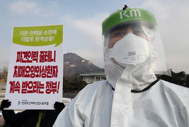 청와대 분수대 앞에서 12일 열린 ‘코로나19 전담병원 보건의료노동자 이탈 실태 발표 및 대책 마련 촉구 기자회견’에서 한 참석자가 방호용구 차림을 하고 있다. 연합뉴스