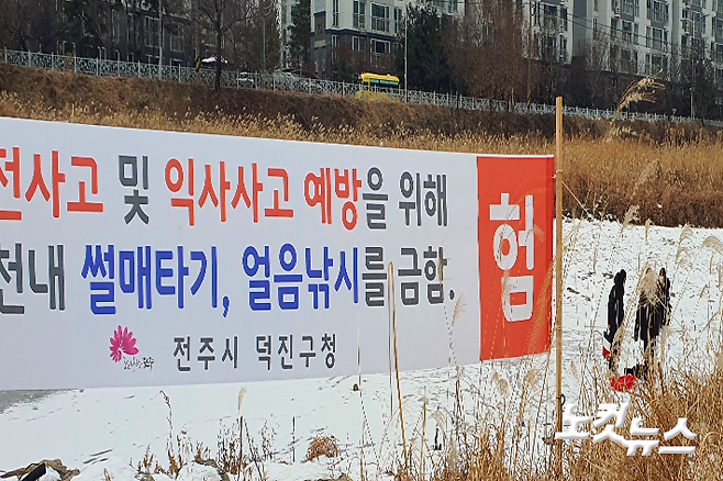 하천에서 '썰매타기와 얼음낚시를 금지한다'는 현수막 너머로 눈썰매를 타는 시민들. 남승현 기자