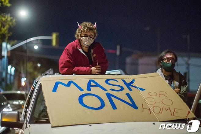 EDITORS NOTE: Graphic content / (FILES) In this file photo taken on December 30, 2020 Protesters wearing face masks stand on their vehicle as they participate along with homeless advocates in a protest against Christian musician Sean Feucht as he plans to hold a public event in Skid Row in spite of the rise of Covid-19 cases in the region, in Los Angeles, California. - The United States has recorded more than 20 million cases of Covid-19, Johns Hopkins University said January 1, 2020 in its real-time tally, as the New Year brought another grim milestone underlining the country's struggle to quell the virus. (Photo by RINGO CHIU / AFP)