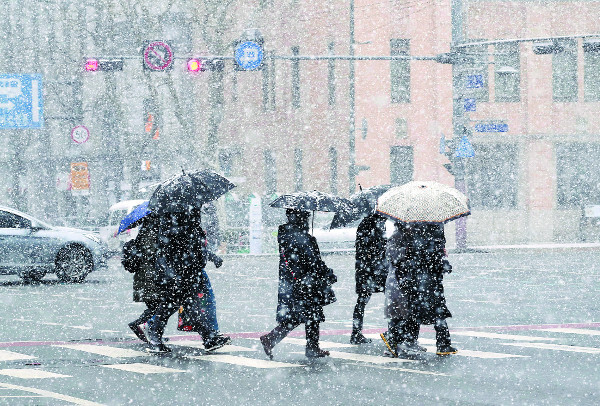 두꺼운 옷차림을 한 시민들이 18일 눈 내리는 서울 종로구 광화문 사거리에서 우산을 쓴 채 횡단보도를 건너고 있다. 기상청은 전국에 깜짝 한파가 찾아온 뒤 20일 오후부터는 당분간 포근한 날씨가 이어질 것이라고 예보했다. 연합뉴스