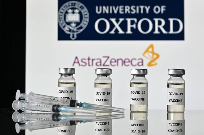 영국 옥스퍼드대와 아스트라제네카의 로고를 배경으로 코로나 백신 스티커가 부착된 병과 주사기가 놓여있는 모습./AFP 연합뉴스