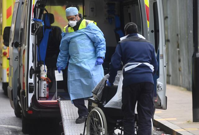26일(현지시간) 영국 런던에 있는 로얄 런던 병원 밖에서 의료진이 구급차에 실려 온 코로나19 확진자를 병원으로 옮기고 있다. 런던=EPA 연합뉴스