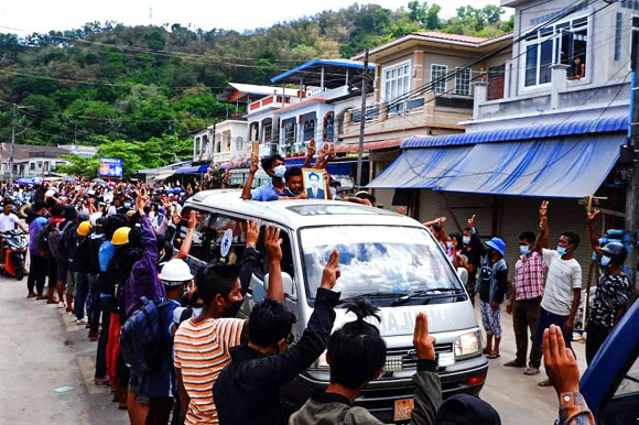 시위 사망자 장례행렬에 ‘세 손가락 경례’하는 미얀마 주민들 - 미얀마 남단 꼬따웅에서 28일(현지시간) 주민들이 전날 군부 쿠데타 규탄 시위 도중 군경이 쏜 총에 맞아 숨진 시위대의 장례 행렬을 향해 ‘세 손가락 경례’를 하고 있다. 세 손가락 경례는 독재에 대한 저항을 상징한다. 미얀마에서는 전날 하루에만 114명의 시위대가 숨져 지난달 1일 발발한 쿠데타 이후 누적 사망자 수는 450명에 달하는 것으로 집계됐다.(다웨이 워치 제공) 2021.3.29 AFP 연합뉴스