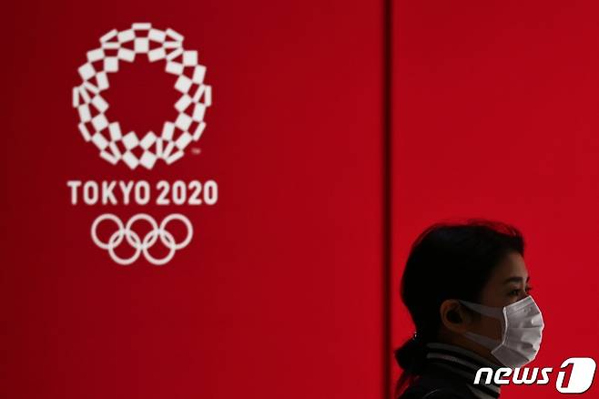 일본 도쿄의 한 거리에서 마스크를 쓴 행인이 도쿄올림픽 로고 앞을 지나가고 있다. © AFP=뉴스1