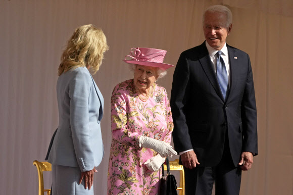 조 바이든(오른쪽) 미국 대통령이 13일(현지시간) 영국 런던 근교 윈저성에서 엘리자베스 2세 여왕과 환담하는 부인 질 바이든을 지켜보며 미소를 짓고 있다. 바이든 대통령은 이날 “여왕의 외모와 그 너그러움이 어머니를 떠올리게 한다”며 여왕을 백악관으로 초청했다고 밝혔다.런던 AP 연합뉴스