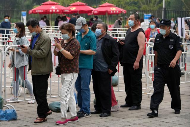 중국 보안요원이 지난 2일 베이징에서 코로나 백신을 맞기 위해 줄을 서 있는 주민들을 힐끗 쳐다보며 지나가고 있다. 베이징=AP 연합뉴스