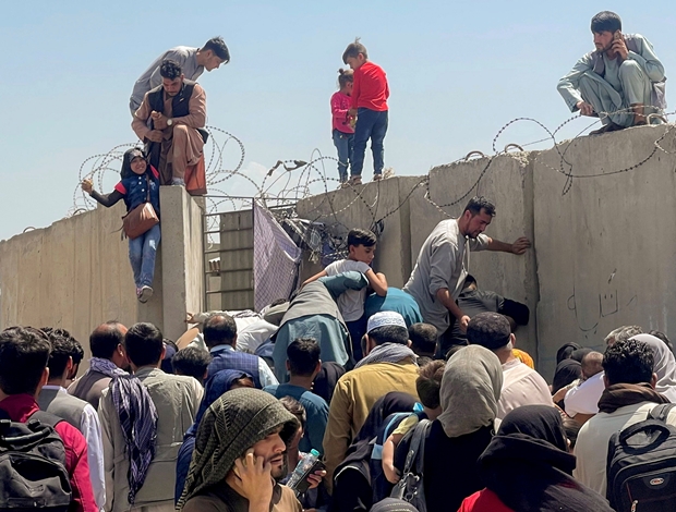 16일 카불공항 주변으로 몰려든 피난민이 철조망이 둘러진 담벼락을 넘어 필사의 탈출을 감행하고 있다./로이터 연합뉴스
