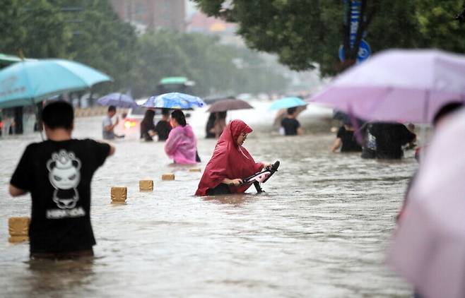 지난 7월20일 중국 정저우에 폭우가 쏟아지는 가운데 시민들이 물에 잠긴 거리를 걷고 있다. AP 연합뉴스