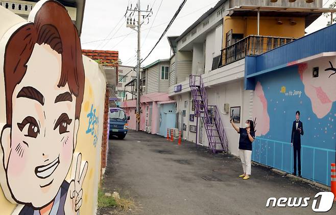 경북 김천예고 옆 교동연화지로 가는 골목길에 조성된 '트바로티 김호중 소리길'에서 팬카페 '아리스' 한 회원이 담장 벽화에 그려진 김호중의 그림을 카메라에 담고 있다. 2021.9.20/뉴스1 © News1 정우용 기자