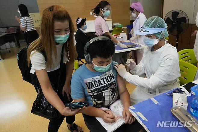 [방콕(태국)=AP/뉴시스]태국 방콕의 한 병원에서 21일 코로나19 백신을 접종받은 한 아이의 어머니가 옆에서 아들에게 휴대전화 화면을 보여주고 있다. 태국 보건 당국이 21일 기저질환이 있는 12∼18세의 아이들에게 화이자의 코로나19 백신을 접종하기로 결정했다. 2021.9.21