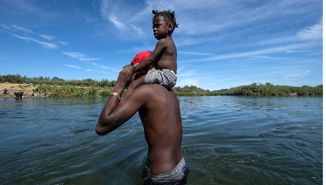 멕시코를 통해 미국으로 온 한 아이티 난민이 22일(현지시각) 음식과 물을 얻기 위해 딸을 목에 태우고 리오 그란데강을 건너 멕시코 쪽으로 가고 있다. AFP=연합뉴스