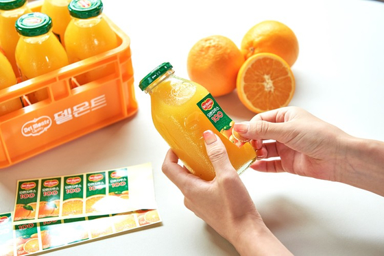 Del Monte's merchandise featuring six orange juice glass bottles and a plastic crate with the juice maker's logo. [LOTTE CHILSUNG BEVERAGE]