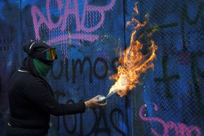 한 멕시코시티 시위 여성이 28일 경찰의 저지 철벽에 불을 쏘고 있다. 로이터=연합뉴스