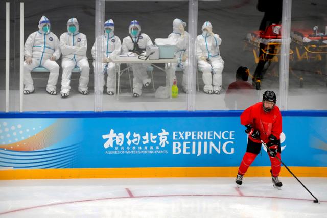 방호복을 입은 중국 방역요원들이 10일 베이징의 아이스하키 경기장에서 내년 2월 동계올림픽을 앞두고 시설 최종 점검에 나선 선수를 지켜보고 있다. 베이징=AP 연합뉴스