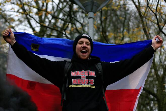 네덜란드 위트레흐트 시민들이 4일 코로나 19 방역조치에 반대하는 시위를 벌였다. 한 참가자가 국기를 펼치고 환호하고 있다. 가슴에 "백신=선택"이라는 글씨를 새겼다. 로이터=연합뉴스