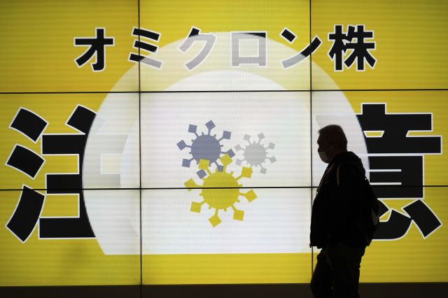 일본 도쿄 시민이 13일 코로나19 변이 오미크론 확산에 대한 주의를 요청하는 안내판 앞을 지나고 있다. AP연합뉴스