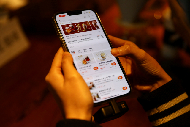 중국 미디어의 한 기자가 18일 중국 베이징의 스타벅스 매장에서 열린 스타벅스와 메이투안의 제휴 행사에서 휴대폰으로 스타벅스 메뉴를 확인하고 있다. /로이터연합