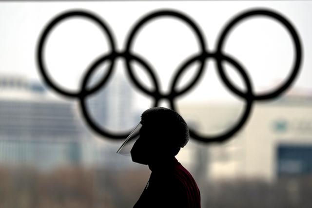 19일 중국 수도 베이징의 2022 동계올림픽 메인 미디어센터 안에서 한 관계자가 얼굴 가리개를 쓴 채 오륜 조형물 앞을 지나고 있다. 베이징=AP 연합뉴스