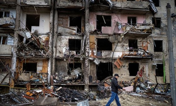 25일(현지시간) 우크라이나 키예프에서 주민들이 러시아의 로켓 공격으로 파손된 건물 앞을 지나고 있다. [AP=뉴시스]