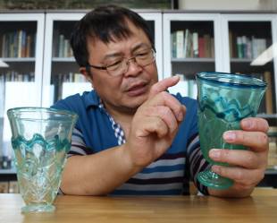 Park Cheun-soo, a professor and director of the Silk Road Survey & Research Center at the Kyungpook National University in Daegu, holds up a glass cup with fishnet pattern that was excavated from a tomb in Kara-Agachi, Kazakhstan. The design on a glass cup excavated in 1926 from Seobongchong matches the fishnet pattern on this piece.