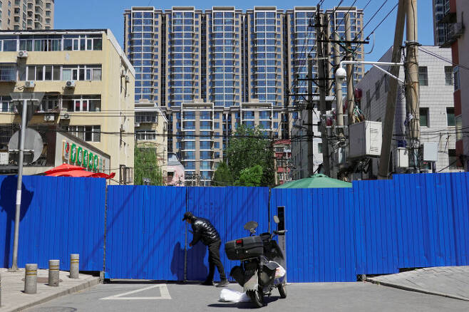 중국 수도 베이징에서 지난 13일 한 남성이 코로나19 확산 방지를 위해 주거지역 주위에 둘러쳐진 바리케이드 사이로 물건을 전달하고 있다. 로이터연합뉴스