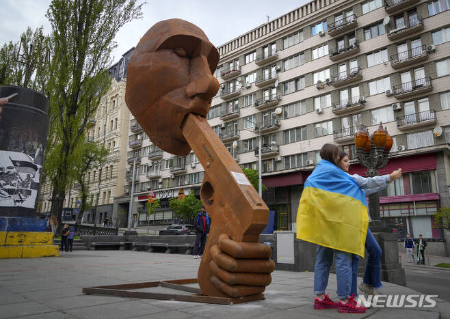[키이우( 우크라이나)= AP/뉴시스] 우크라이나 수도 키이우 중심가에 설치된 블라디미르 푸틴 러시아 대통령 조각상 앞에서 지난 7일(현지시간) 우크라이나 국기를 두른 여성들이 사진을 찍고 있다. 2022.05.24.