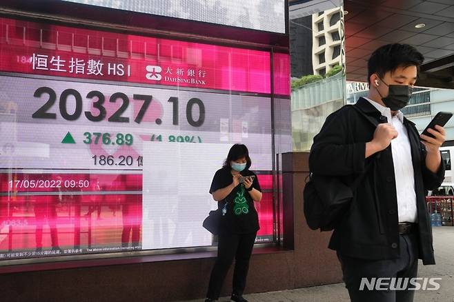 [홍콩=AP/뉴시스] 코로나19 예방을 위해 마스크를 착용한 홍콩 시민들이 17일 증권 시세 전광판 앞에서 스마트폰을 열심히 보고 있다. 2022.05.18