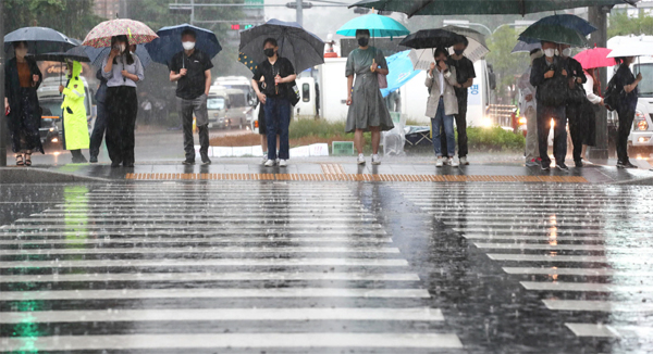 전국적으로 장마가 시작된 23일 서울 광화문에 폭우가 쏟아지는 가운데 시민들이 우산을 쓰고 신호등이 바뀌기를 기다리고 있다. [이충우 기자]