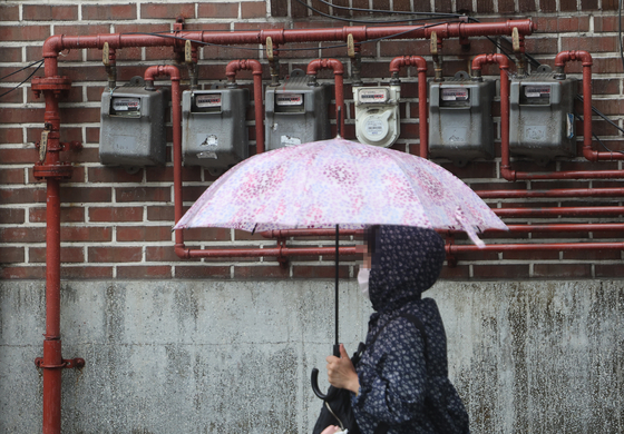 A pedestrian walks past electricity meters on a building in Seoul on Thursday. Public utility fees for both electricity and gas will go up starting July. [YONHAP]