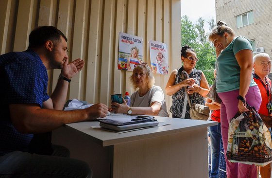 러시아가 점령한 우크라이나 남부 헤르손시 주민들이 지난달 25일 러시아 시민권과 여권을 취득하기 위해 서류를 제출하고 있다. 벽에 걸린 포스터에는 "러시아는 영원히 여기에 있다"라고 쓰여 있다. 로이터=연합뉴스