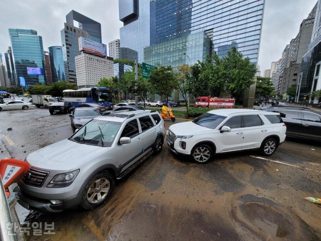 9일 오전 서울 강남역 진흥아파트 부근 사거리에 폭우로 인해 방치된 차량을 출근 차량들이 아슬아슬하게 비켜 지나가고 있다. 김재현 기자