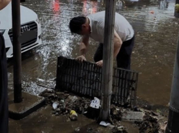 실시간 강남역 슈퍼맨 - 침수된 강남역 인근에서 한 남성이 8일 혼자 맨손으로 도로변 배수관 덮개를 열어 쌓여 있던 쓰레기를 치우고 있다. 직후 도로에 고인 물이 순식간에 빠졌다. 온라인커뮤니티 캡처