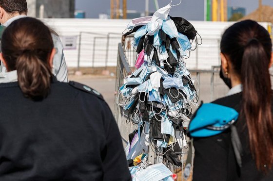 지난 1월 3일 이스라엘 지중해 연안 도시 헤르츨리야에서 버려진 마스크를 모아서 걸어놓은 울타리 옆을 여성 경찰관들이 지나가고 있다. AFP=연합뉴스