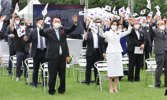 President Yoon Suk-yeol, left, and first lady Kim Keon-hee wave Korean flags during a ceremony marking the 77th Liberation Day on the front lawn of the presidential office in Yongsan District, central Seoul, on Monday. [YONHAP]