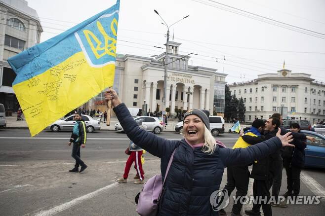우크라이나 국기 흔들며 기뻐하는 헤르손 주민들 (헤르손 AP=연합뉴스) 12일(현지시간) 우크라이나 헤르손 시내에서 주민들이 우크라이나 국장이 그려진 깃발을 들고 탈환을 축하하고 있다. 헤르손은 지난 9월 러시아가 주도한 주민투표로 러시아에 병합됐으나, 러시아군이 드니프로 강 동안으로 철수함에 따라 우크라이나군에 의해 수복됐다. 우크라이나 당국은 주민들의 안전을 보장하기 위한 '안정화 대책'을 강구 중이라고 전했다. 2022.11.13 alo95@yna.co.kr