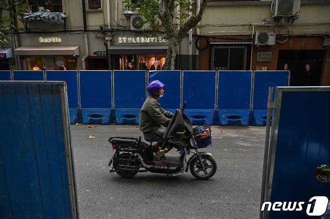 28일 중국 상하이 소재 우루무치 대로 주변에 설치된 바리케이드 옆을 시민들이 오토바이로 이동하고 있다.ⓒ AFP=뉴스1