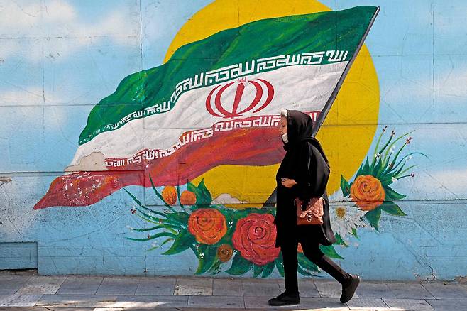 2022년 10월 11일 한 여성이 이란 수도 테헤란의 벽화를 지나가고 있다. 도덕 경찰은  여성이 머리카락을 히잡으로 제대로 가리지 않거나, 몸에 딱 붙는 옷을 착용할 경우 단속한다.  지난 9월 의문사한 마흐사 아미니(22) 역시 히잡을 제대로 쓰지 않았다는 이유로 도덕 경찰에 끌려갔다가 목숨을 잃었다. ./AFP연합뉴스