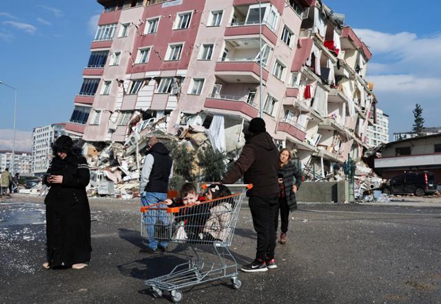 7일 튀르키예 하타이에서 시민들이 전날 발생한 지진으로 무너진 건물 앞에 서 있다. 하타이=로이터 연합뉴스
