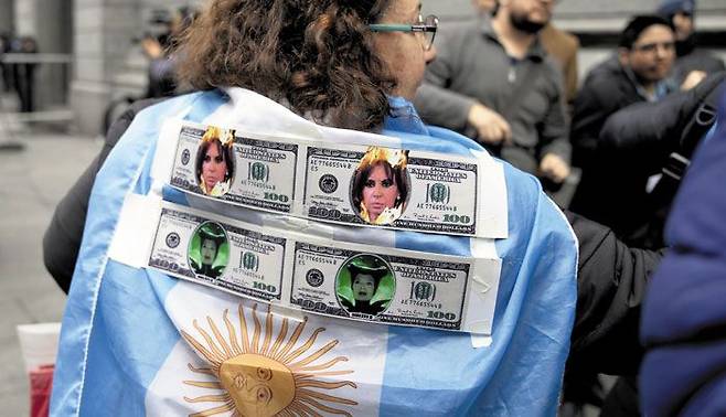 아르헨티나 수도 부에노스아이레스에서 열린 최근 시위에서 한 여성이 미국 달러와 크리스티나 페르난데스 부통령 등 정부 관계자의 얼굴을 합성한 사진을 등에 붙이고 행진하고 있다. 시위자들은 정부 재정 적자에 아랑곳 않고 보조금 인상 등 정부에 더 많은 ‘퍼주기’를 요구했다./AP연합뉴스