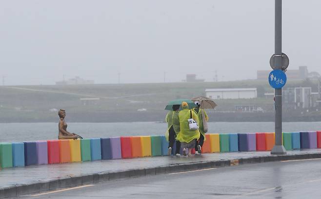지난 25일 제주시 도두동 무지개 해안도로에서 관광객들이 비옷을 입고 우산을 쓴 채 길을 걷고 있다. /연합뉴스