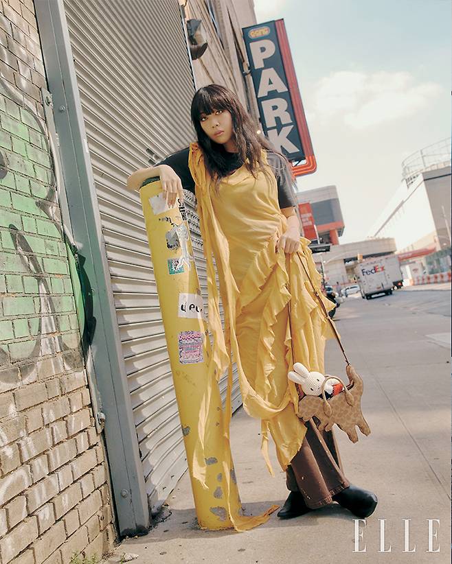 공룡 모티프의 시그니처 캔버스 렉시 백과 시폰 소재의 옐로 드레스와 매치한 티셔츠, 팬츠는 모두 Coach.