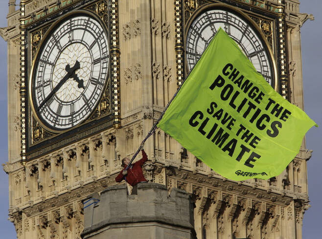 환경단체 그린피스 활동가가 영국 런던 랜드마크인 시계탑 빅벤에 올라 ‘기후를 살리려면 정치를 바꾸자’라고 쓰인 대형 깃발을 휘두르며 기후변화 대응 촉구 시위를 벌이고 있다. [그린피스 영국]